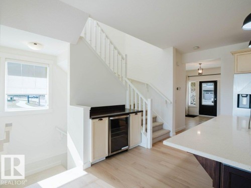 Open concept main level featuring a light wood-finish flooring, white staircase with carpeted treads, and a built-in beverage center with a dark countertop and two-tone cabinetry - 15867 11 Avenue, Edmonton, AB - Indoor
