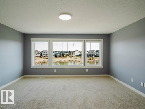 Spacious room featuring three large picture windows, neutral wall paint, and plush carpeting - 15867 11 Avenue, Edmonton, AB - Indoor Photo Showing Other Room