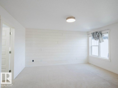 Spacious interior room featuring a shiplap accent wall, light-colored carpet flooring, and a single window with white trim - 15867 11 Avenue, Edmonton, AB - Indoor Photo Showing Other Room