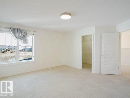 Bright room featuring plush carpeting, a large window, a ceiling-mounted light fixture, and a walk-in closet with built-in shelving - 15867 11 Avenue, Edmonton, AB - Indoor Photo Showing Other Room