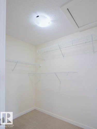 Walk-in closet featuring carpet flooring, white wire shelving, a ceiling-mounted light fixture, and a white access panel - 15867 11 Avenue, Edmonton, AB - Indoor With Storage
