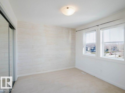 Room featuring light-toned plank-style accent wall, dual windows with roller shades, neutral carpeting, and a mirrored sliding closet door - 15867 11 Avenue, Edmonton, AB - Indoor Photo Showing Other Room