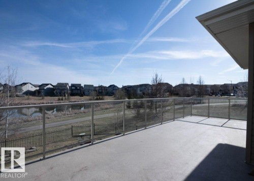 Spacious outdoor concrete deck featuring a glass railing system and a pond backdrop - 15867 11 Avenue, Edmonton, AB - Outdoor With View