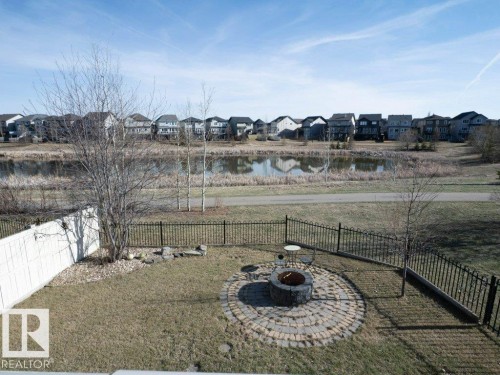 Backyard featuring a paver patio with fire pit, perimeter fencing, and a waterfront backdrop - 15867 11 Avenue, Edmonton, AB - Outdoor With View