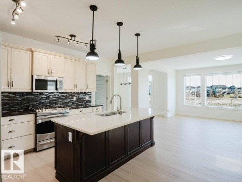 Open-concept kitchen featuring light-toned cabinetry, a stainless steel range and microwave, and a dark mosaic tile backsplash - 15867 11 Avenue, Edmonton, AB - Indoor Photo Showing Kitchen With Double Sink With Upgraded Kitchen