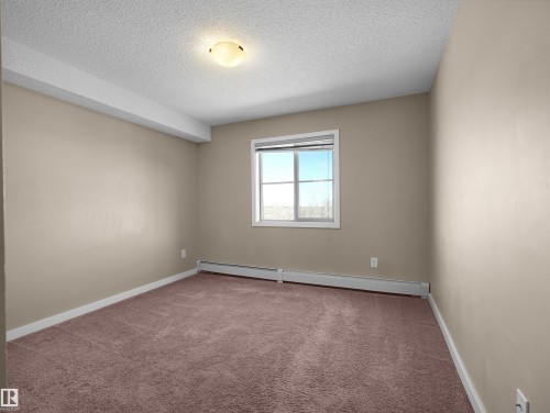 Spacious room featuring neutral painted walls, light brown carpeting, a window with natural light, and a ceiling-mounted light fixture - 417 1060 Mcconachie Boulevard, Edmonton, AB - Indoor Photo Showing Other Room