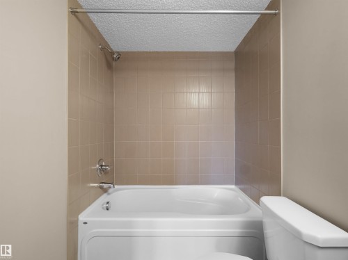 White bathtub and shower combination with chrome fixtures, tan tile surround, and a textured ceiling - 417 1060 Mcconachie Boulevard, Edmonton, AB - Indoor Photo Showing Bathroom