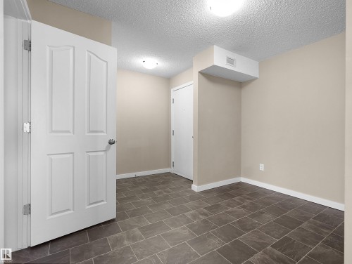 Rectangular tile flooring complements neutral-toned walls, contrasting with white trim and a white paneled door - 417 1060 Mcconachie Boulevard, Edmonton, AB - Indoor Photo Showing Other Room