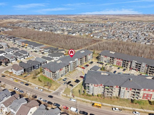 Modern multi-story apartment building featuring a dark gray shingle roof and a red and gray facade - 417 1060 Mcconachie Boulevard, Edmonton, AB - Outdoor With View