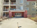 Building exterior featuring a stone facade, multi-story balconies with black railings, a prominent main entrance with glass doors, and a concrete pathway - 417 1060 Mcconachie Boulevard, Edmonton, AB  - Outdoor With Balcony 