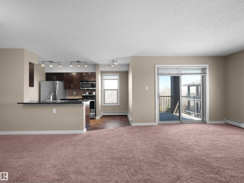 Spacious living area featuring neutral-toned walls, plush carpeting, and baseboard heating - 417 1060 Mcconachie Boulevard, Edmonton, AB - Indoor Photo Showing Other Room