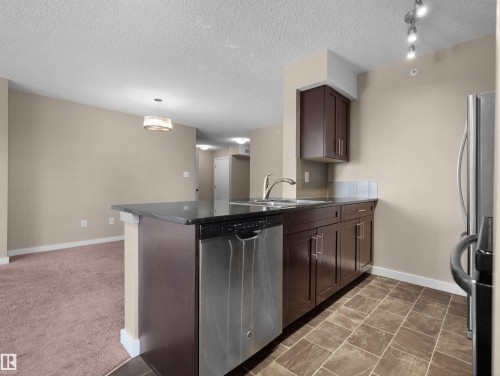 Kitchen featuring dark wood cabinetry, a stainless steel dishwasher, and a double basin sink with a gooseneck faucet - 417 1060 Mcconachie Boulevard, Edmonton, AB - Indoor Photo Showing Kitchen