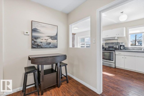 Kitchen featuring wood-finish flooring, white cabinetry, dark countertops, a stainless steel range, and a pass-through window to an adjacent space - 13107 133 Street, Edmonton, AB - Indoor Photo Showing Other Room