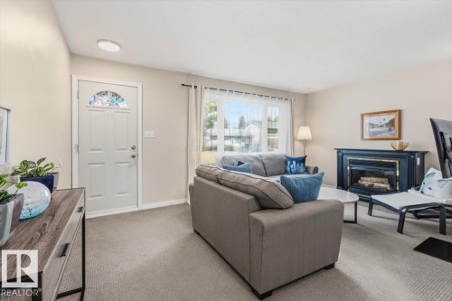 Inviting living space featuring light-toned carpeting, a decorative fireplace with a dark mantel, and a front entry door with an arched decorative glass insert - 13107 133 Street, Edmonton, AB - Indoor Photo Showing Living Room With Fireplace