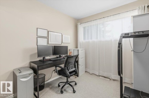 Carpeted room featuring a large window with sheer white curtains, light neutral wall color, and a built-in air vent - 13107 133 Street, Edmonton, AB - Indoor Photo Showing Office