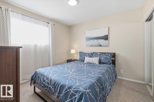 Bedroom featuring textured carpet flooring, neutral wall tones, a window with sheer and patterned drapes, and a mirrored closet - 13107 133 Street, Edmonton, AB - Indoor Photo Showing Bedroom