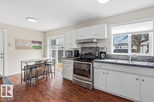 Bright kitchen featuring wood-finish flooring, white cabinetry, stainless steel appliances, and a double basin sink - 13107 133 Street, Edmonton, AB - Indoor Photo Showing Kitchen With Double Sink