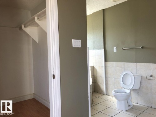 Bathroom featuring a floor-mounted toilet, light-toned ceramic tile flooring, and half-height wall tiling - 11507 141 Avenue, Edmonton, AB - Indoor Photo Showing Bathroom