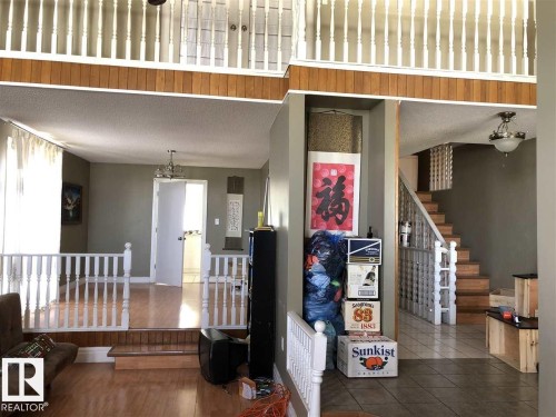 Multi-level interior featuring wood-finish flooring, a white spindle railing system, a chandelier light fixture, an open-tread staircase with wood risers, and a tiled entry area - 11507 141 Avenue, Edmonton, AB - Indoor Photo Showing Other Room