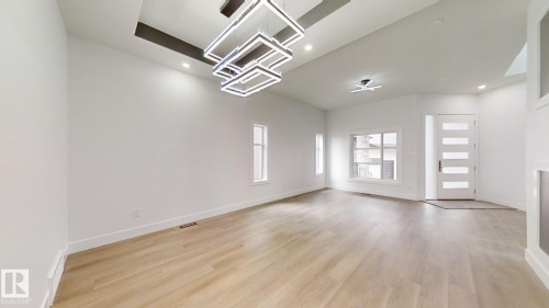 Spacious room featuring light wood-finish flooring, white walls, and a recessed ceiling detail with a multi-tiered contemporary light fixture - 1707 18 Street Nw, Edmonton, AB - Indoor Photo Showing Other Room