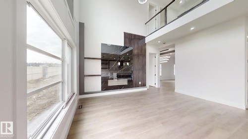 Spacious open-concept interior featuring light wood-finish flooring, a two-story ceiling, and a prominent dark marble-look fireplace surround with built-in shelving - 1707 18 Street Nw, Edmonton, AB - Indoor Photo Showing Other Room