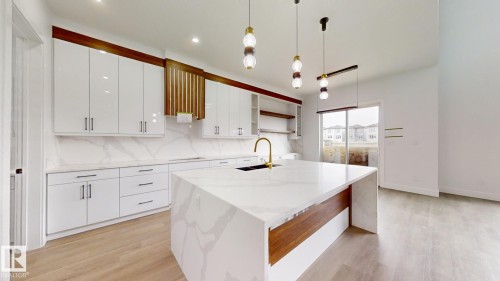 Modern kitchen featuring a waterfall-edge island with integrated sink, white high-gloss cabinetry, wood-finish accents, and pendant lighting - 1707 18 Street Nw, Edmonton, AB - Indoor Photo Showing Kitchen With Upgraded Kitchen