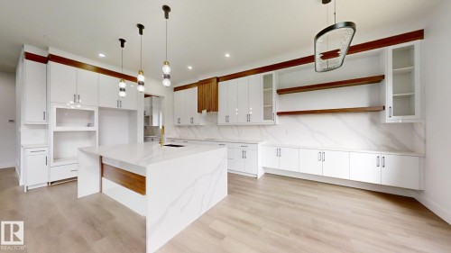 Kitchen featuring a waterfall-edge island with integrated sink, white cabinetry with wood-finish accents, full-height backsplash, gold-toned hardware, and pendant lighting - 1707 18 Street Nw, Edmonton, AB - Indoor Photo Showing Kitchen