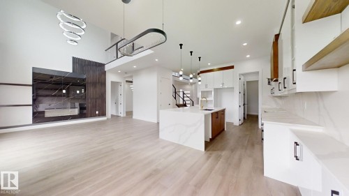 Open-concept living space featuring high ceilings, wood-finish flooring, a contemporary kitchen island with a gold-tone faucet, white cabinetry with black hardware, and a striking dark marble-effect accent wall - 1707 18 Street Nw, Edmonton, AB - Indoor Photo Showing Kitchen