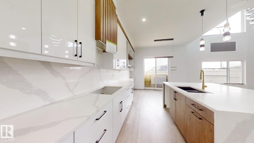 Contemporary kitchen featuring white high-gloss cabinetry, quartz countertops with integrated backsplash, and a central island with wood-finish base cabinetry - 1707 18 Street Nw, Edmonton, AB - Indoor Photo Showing Kitchen With Double Sink With Upgraded Kitchen