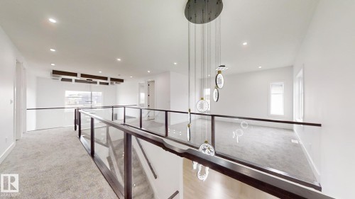 Spacious upper-level landing featuring light gray carpeting, glass panel railings with dark wood-finish tops, recessed ceiling lighting, and a multi-pendant chandelier - 1707 18 Street Nw, Edmonton, AB - Indoor Photo Showing Other Room