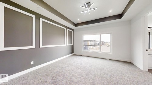 Spacious room featuring tray ceiling with accent lighting, contemporary chandelier, large window, textured carpeting, and decorative wall molding - 1707 18 Street Nw, Edmonton, AB - Indoor Photo Showing Other Room