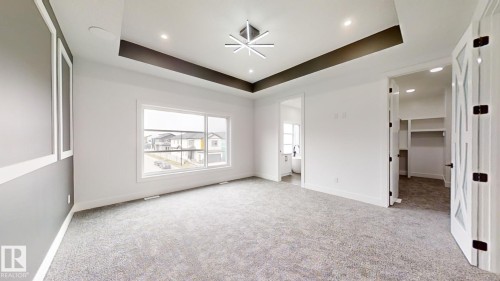 Spacious room featuring a tray ceiling with recessed lighting and a modern chandelier, large window, patterned accent wall, and a walk-in closet with built-in shelving - 1707 18 Street Nw, Edmonton, AB - Indoor Photo Showing Other Room