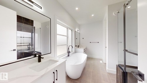 Contemporary bathroom featuring a freestanding tub, dual vanities with integrated sinks and black hardware, a glass-enclosed shower with black trim, and wood-finish herringbone flooring - 1707 18 Street Nw, Edmonton, AB - Indoor Photo Showing Bathroom