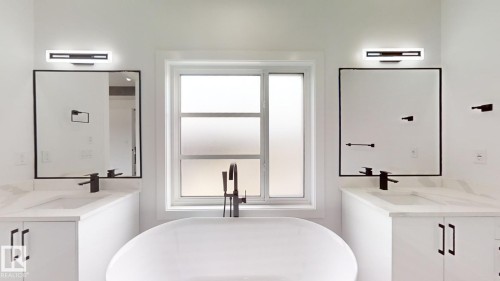 Soaking tub with a floor-mounted matte black faucet, flanked by dual vanities with integrated sinks, white countertops, and matte black fixtures - 1707 18 Street Nw, Edmonton, AB - Indoor Photo Showing Bathroom