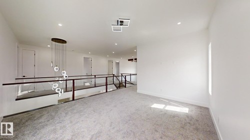 Spacious upper-level landing featuring a contemporary tiered chandelier, recessed lighting, glass panel railing with dark wood handrails, light gray carpeting, and multiple interior doors - 1707 18 Street Nw, Edmonton, AB - Indoor Photo Showing Other Room