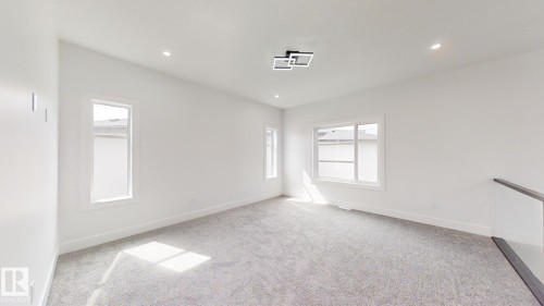 Spacious room featuring light gray carpeting, multiple windows, a modern ceiling light fixture, recessed lighting, and a glass-paneled railing - 1707 18 Street Nw, Edmonton, AB - Indoor Photo Showing Other Room
