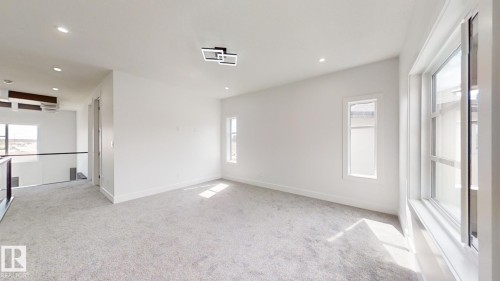 Spacious open area featuring light gray carpeting, recessed ceiling lighting, a modern rectangular flush-mount light fixture, and multiple windows with white trim - 1707 18 Street Nw, Edmonton, AB - Indoor Photo Showing Other Room