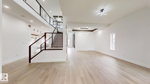 Open-concept living space featuring light wood-finish flooring, a contemporary floating staircase with glass railings, white walls, and modern ceiling light fixtures - 1707 18 Street Nw, Edmonton, AB - Indoor Photo Showing Other Room