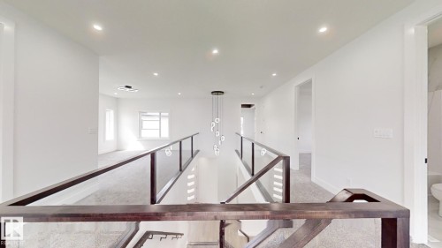 Upper-level landing featuring glass panel railing, recessed ceiling lighting, a modern multi-pendant chandelier, and light gray carpeting - 1707 18 Street Nw, Edmonton, AB - Indoor Photo Showing Other Room