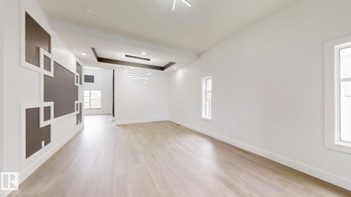 Spacious room featuring light wood-finish flooring, white walls, and a contemporary linear chandelier - 1707 18 Street Nw, Edmonton, AB - Indoor Photo Showing Other Room