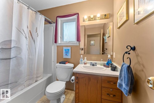 Full bathroom featuring a white tub/shower combination, a toilet, and a vanity with a white countertop and wood-finish cabinetry - 1414 7 Avenue, Cold Lake, AB - Indoor Photo Showing Bathroom