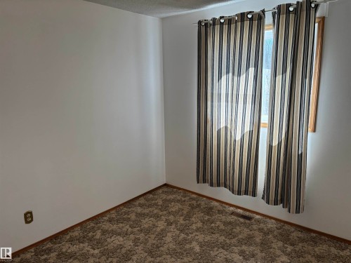 Room featuring a window with striped drapes, textured carpeting, white walls, and wood trim - 4824 49 Avenue, Sangudo, AB - Indoor Photo Showing Other Room