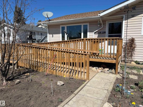 Ranch-style residence featuring light-colored siding, a brown shingle roof, and a prominent wood-finish deck with an integrated ramp - 4824 49 Avenue, Sangudo, AB - Outdoor