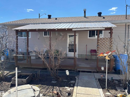 Rear exterior featuring light-colored siding, a covered wooden deck, and a concrete pathway - 4824 49 Avenue, Sangudo, AB - Outdoor