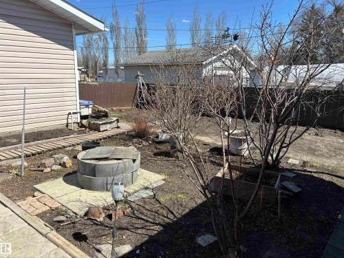 Expansive outdoor space featuring a circular concrete block fire pit, concrete pavers, and a wooden pathway - 4824 49 Avenue, Sangudo, AB - Outdoor
