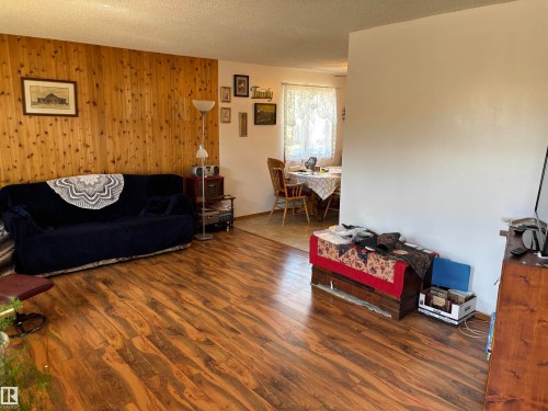 Spacious room featuring wood-finish flooring, a full-height wood panel accent wall, and painted walls - 4824 49 Avenue, Sangudo, AB - Indoor Photo Showing Living Room