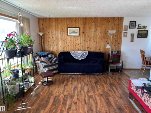 Interior living area featuring wood-finish flooring, a prominent wood accent wall, and textured ceiling - 4824 49 Avenue, Sangudo, AB - Indoor Photo Showing Living Room
