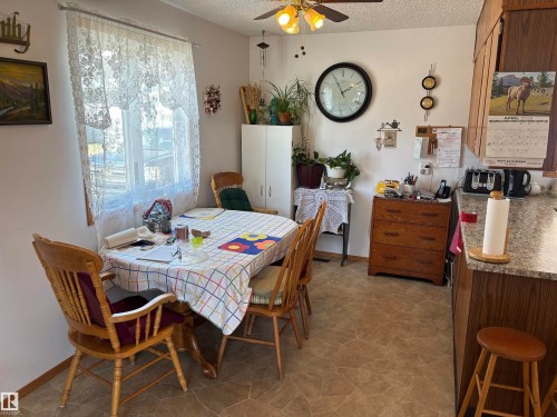 Kitchen/dining area with a large window, ceiling fan with integrated lighting, wood-finish cabinetry, and a stone-look countertop - 4824 49 Avenue, Sangudo, AB - Indoor Photo Showing Dining Room