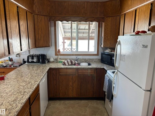 Kitchen featuring wood cabinetry, stone-finish countertops, and a white tile backsplash - 4824 49 Avenue, Sangudo, AB - Indoor Photo Showing Kitchen