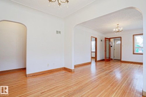 Spacious interior featuring wood-finish flooring, white walls, and decorative chandeliers - 9611 81 Avenue, Edmonton, AB - Indoor Photo Showing Other Room